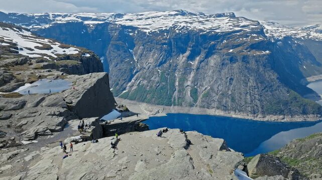 Massive rock ledge overlooking the fjord at Trolltunga, Norway. Drone footage capturing the famous cliff and surrounding mountains above calm blue water.