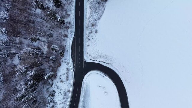 Top-down aerial drone flight moving forward over a snow-covered landscape in Switzerland, showing the main road and a secondary road leading to a village, with a steep gorge on the left.