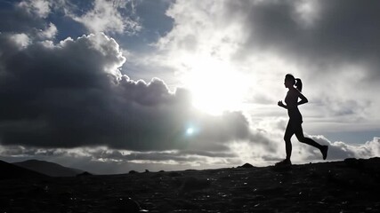 Silhouette runner climbing rocky hill under dramatic sky symbolizing challenge endurance motivation and outdoor fitness