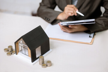 Business Professional Using Tablet and Digital Pen for Real Estate Financial Planning with House Model and Coins
