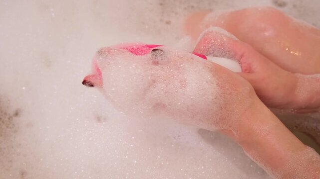 Female hand lowers pink sex toy onto soap suds filling tub, evoking private bathing ritual with added stimulation for ultimate relaxation and personal indulgence