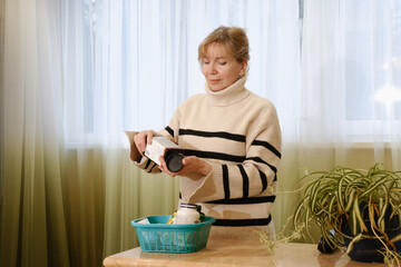 Woman in her 50s organizing dietary supplements and nutrients on kitchen counter, self-care and wellness routine at home. Daily vitamins and supplements for mature people