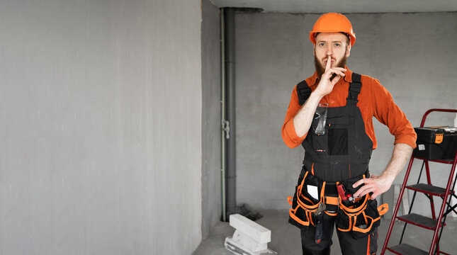 Portrait of bearded male engineer or builder doing shush gesture in building house