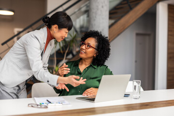 Obraz premium Professional Women Collaborating in Modern Office Setting with Laptops and Documents