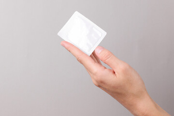 Hand holding Blank white sachet packet mockup on gray background. Empty disposable shampoo or...