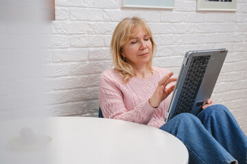 Middle-aged woman browsing on laptop at home, cozy interior scene with copy space, online communication and learning