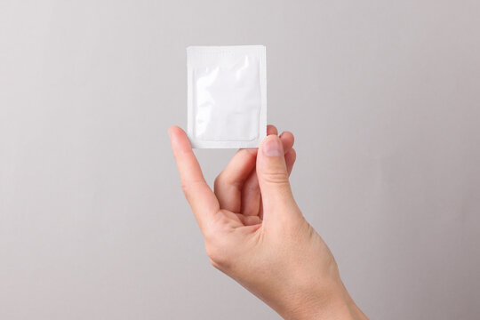 Hand holding Blank white sachet packet mockup on gray background. Empty disposable shampoo or conditioner pack mock up for your design