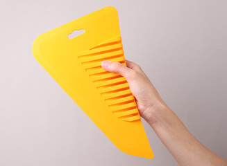 Yellow plastic wallpaper spatula in hand on grey background