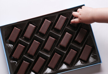 Kid hand holding chocolates in box on white background. Top view