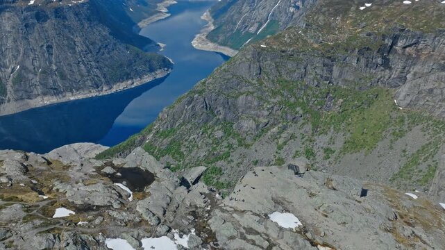 Trolltunga cliff and fjord landscape in Norway seen from above. Cinematic drone shot revealing deep blue water surrounded by steep mountain walls in summer.