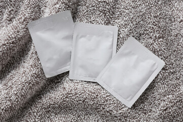 Blank white sachet packets mockup on gray towel. Empty disposable shampoo or conditioner pack mock up