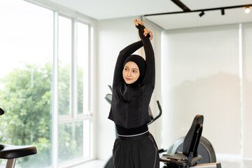 Muslim women wearing sportswear stretching arms in modern gym. Promotes diversity, fitness, active lifestyle. Ideal for wellness, workout, hijab fashion and inclusive health campaigns.
