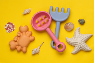 Toy shovel with rake for sandbox and seshells on yellow background. Summel holiday