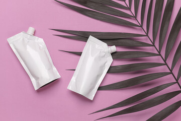 Naklejka premium White Doypacks on pink background with palm leaf