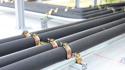 Air conditioning refrigeration pipe. Close-up of black insulated refrigerant pipes lined up and fixed with clamps mounted on concrete floor, copy space with selective focus.