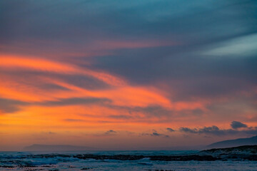 Obraz premium Dramatic Golden sunset over tranquil beach, waves lashing the pebble coastline