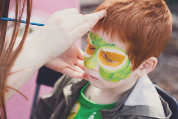Child animator, artist's hand draws face painting to redhead child. Redhead boy with funny face...