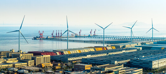 Modern wind turbines and industrial port facility with cargo containers and cranes by the sea. © zhao dongfang