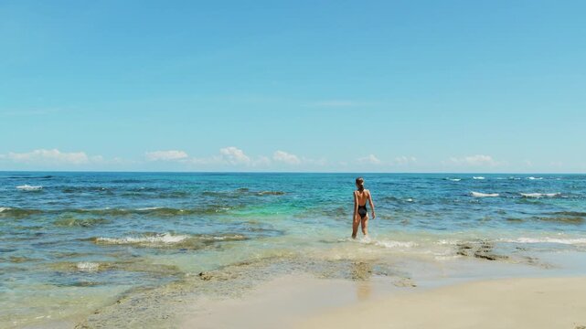Woman walking into shallow ocean water under clear sky on a sunny morning in Costa Rica