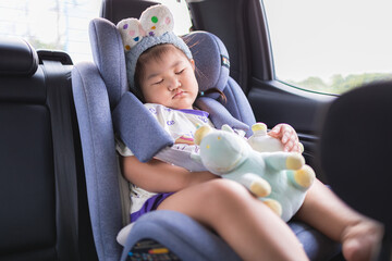 Little Asian girl sleeping peacefully in a car seat during a road trip,A cute young Asian girl wearing a headband is fast asleep in her safety car seat while traveling in a vehicle,