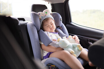 Little Asian girl sleeping peacefully in a car seat during a road trip,A cute young Asian girl wearing a headband is fast asleep in her safety car seat while traveling in a vehicle,