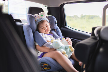 Little Asian girl sleeping peacefully in a car seat during a road trip,A cute young Asian girl wearing a headband is fast asleep in her safety car seat while traveling in a vehicle,