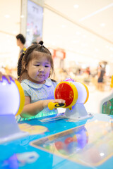 Little Asian girl playing interactive arcade game at indoor playground,A cute little Asian girl with braided hair concentrates on playing a colorful interactive arcade game at a children's amusement 