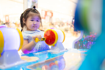 Little Asian girl playing interactive arcade game at indoor playground,A cute little Asian girl with braided hair concentrates on playing a colorful interactive arcade game at a children's amusement 