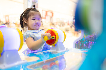 Little Asian girl playing interactive arcade game at indoor playground,A cute little Asian girl with braided hair concentrates on playing a colorful interactive arcade game at a children's amusement 