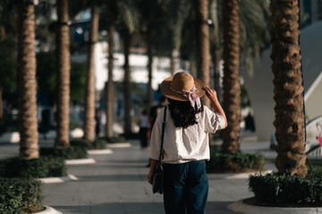 Fototapeta premium Tourist woman walking through palm trees in public park enjoying Dubai city travel