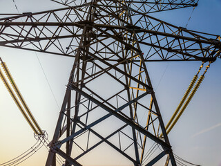 Low angle view of a high voltage electricity pylon tower against a clear blue sky with bright sunlight.