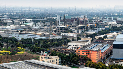 Large chemical plant and oil refinery with storage tanks and industrial buildings under a hazy sky.