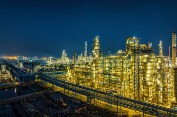 Fototapeta premium Illuminated oil refinery chemical plant with complex pipe systems and storage tanks at night.