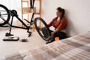 Woman rear wheel adjustment at home. Repairwoman with bicycle in bedroom