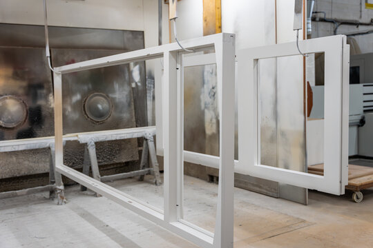 Vue de cadres menuiseries aluminium de vitres blancs dispos&eacute;s en atelier, illustrant un environnement de fabrication ou de pr&eacute;paration de menuiseries avec un aspect industriel et organis&eacute;.