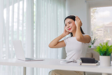 Fototapeta premium Young woman listening to music on white wireless headphones while sitting at a desk with a laptop, smiling