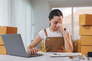 Young Asian woman feeling headache and stressed, experiencing burnout while working on her online e commerce small business