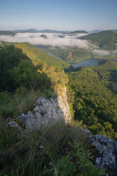 Aerial view of low-lying clouds nestling amidst the rolling green hills and the calm waters of the lake, Sivec, Kosice Region, Slovakia.