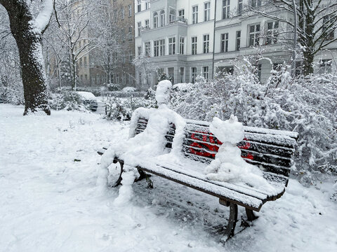 Snowman and Snowdog sitting on a bench in Berlin Kreuzberg on a snowy winter day at Grimmstrasse park.