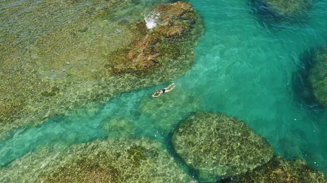 Aerial view of swimmer woman floating in clear turquoise water above reefs in Costa Rica