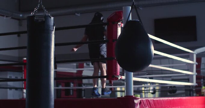 Against soft gym light, the boxer's silhouette flows effortlessly, combining strength and determination in a rhythmic jump rope session. Slow motion zoom out 4K footage.