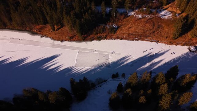Aerial view of the frozen Grubsee in Bavaria. People ice skating and playing hockey in a winter wonderland. Drone shot focusing on active recreation and the beauty of the German Alps