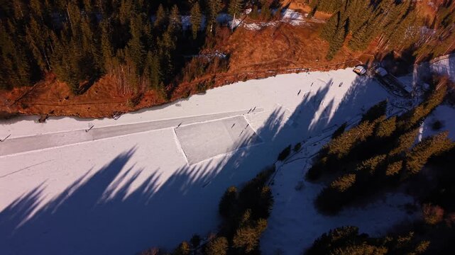 Drone footage of a natural skating rink at Grubsee near Klais. Active people enjoying winter weather on the ice. Majestic snowy peaks and a blue sky create a perfect Bavarian landscape