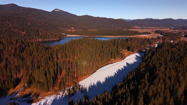 Cinematic drone shot of winter fun at Grubsee lake near Wallgau. People ice skating on the frozen water surrounded by thick snow and alpine peaks. Perfect active vacation in nature