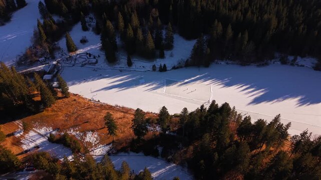 High-angle drone shot of the frozen Grubsee lake in Germany. People enjoying outdoor winter sports, ice skating, and hockey amidst a snowy alpine valley and majestic mountain summits