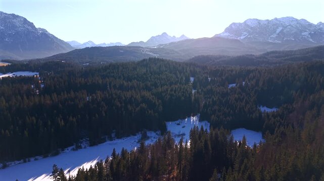 Aerial drone footage of people ice skating and playing hockey on frozen Grubsee lake near Kruen. Sunny winter day in the Bavarian Alps with snow-covered mountains and pine forest scenery