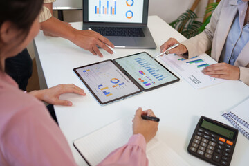 Business team performing data analysis and financial planning using digital tablets and reports during a collaborative office meeting.
