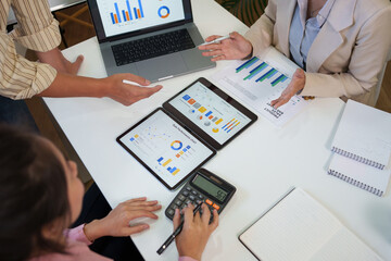 Business professionals performing data visualization analysis and team collaboration using digital tablets and calculator in a bright office environment.