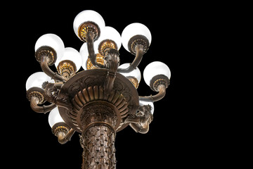 Detailed view looking up at a large antique ornate steel and brass lamp post and lamps against black background, nobody