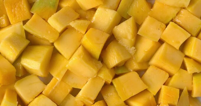 Peeled, ripe mango fruit pieces. Background texture. Table spin.